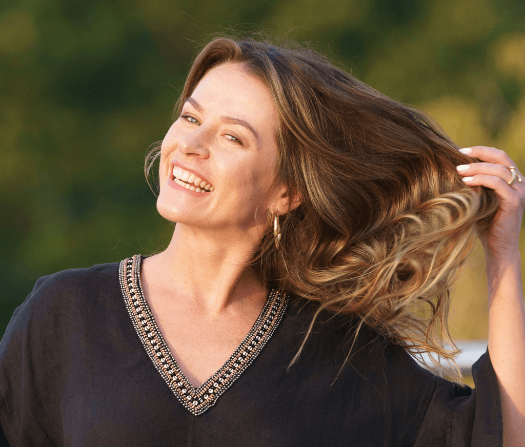 A smiling woman running her fingers tossing her hair after a successful hair restoration treatment