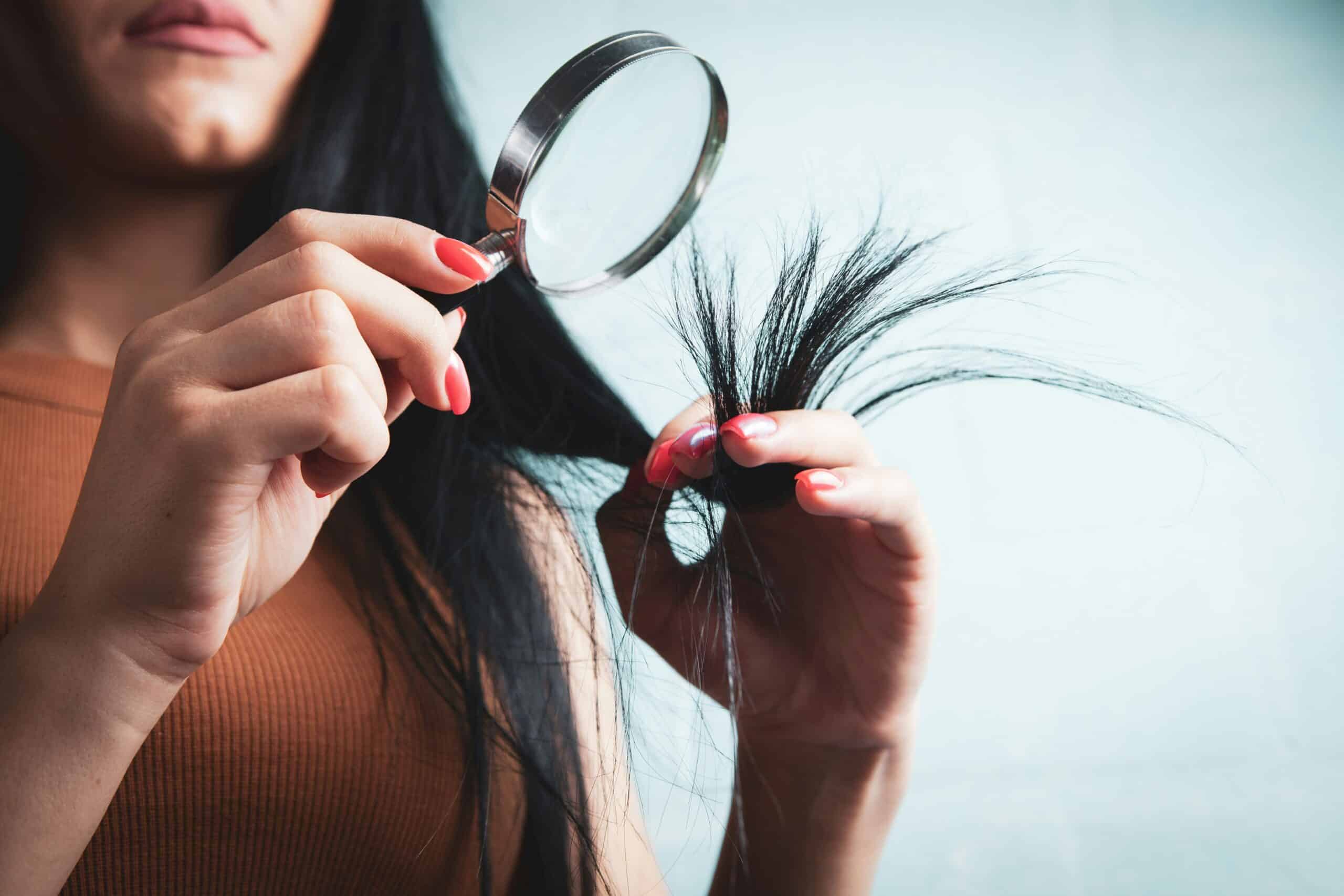 Woman examining her hair with a magnifying glass
